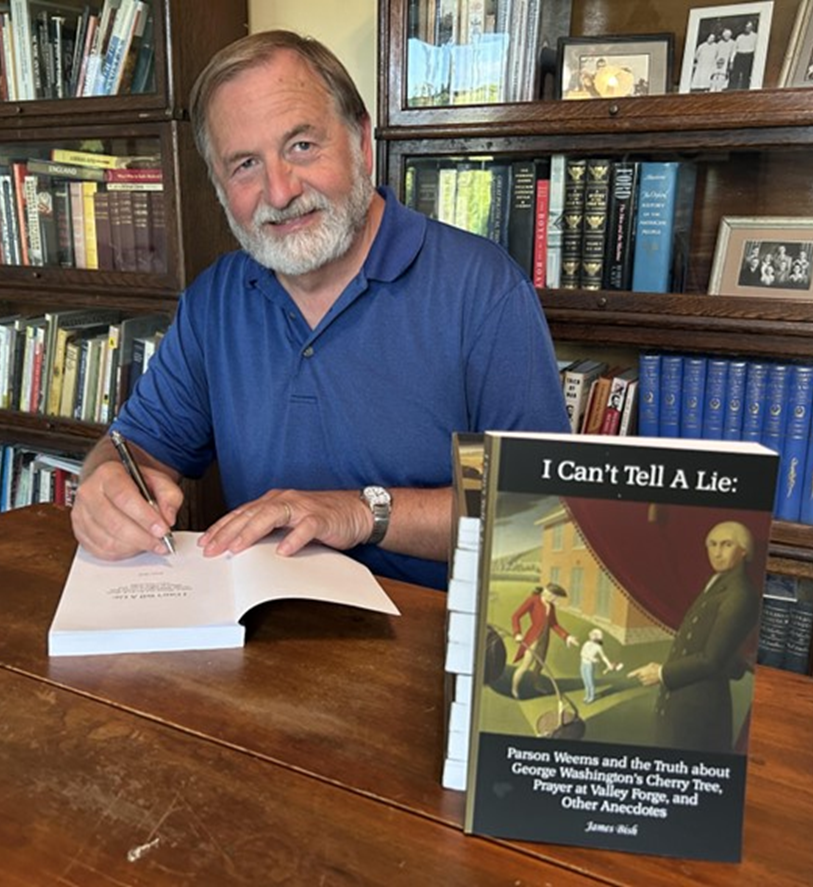 Author signing a book at a wooden desk, shelves with books in the background.