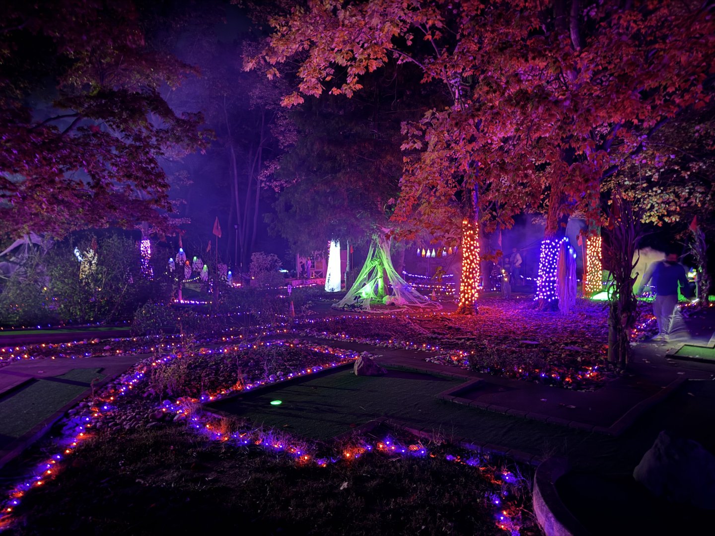 Vibrant mini golf course with colorful lights and Halloween decorations at night.