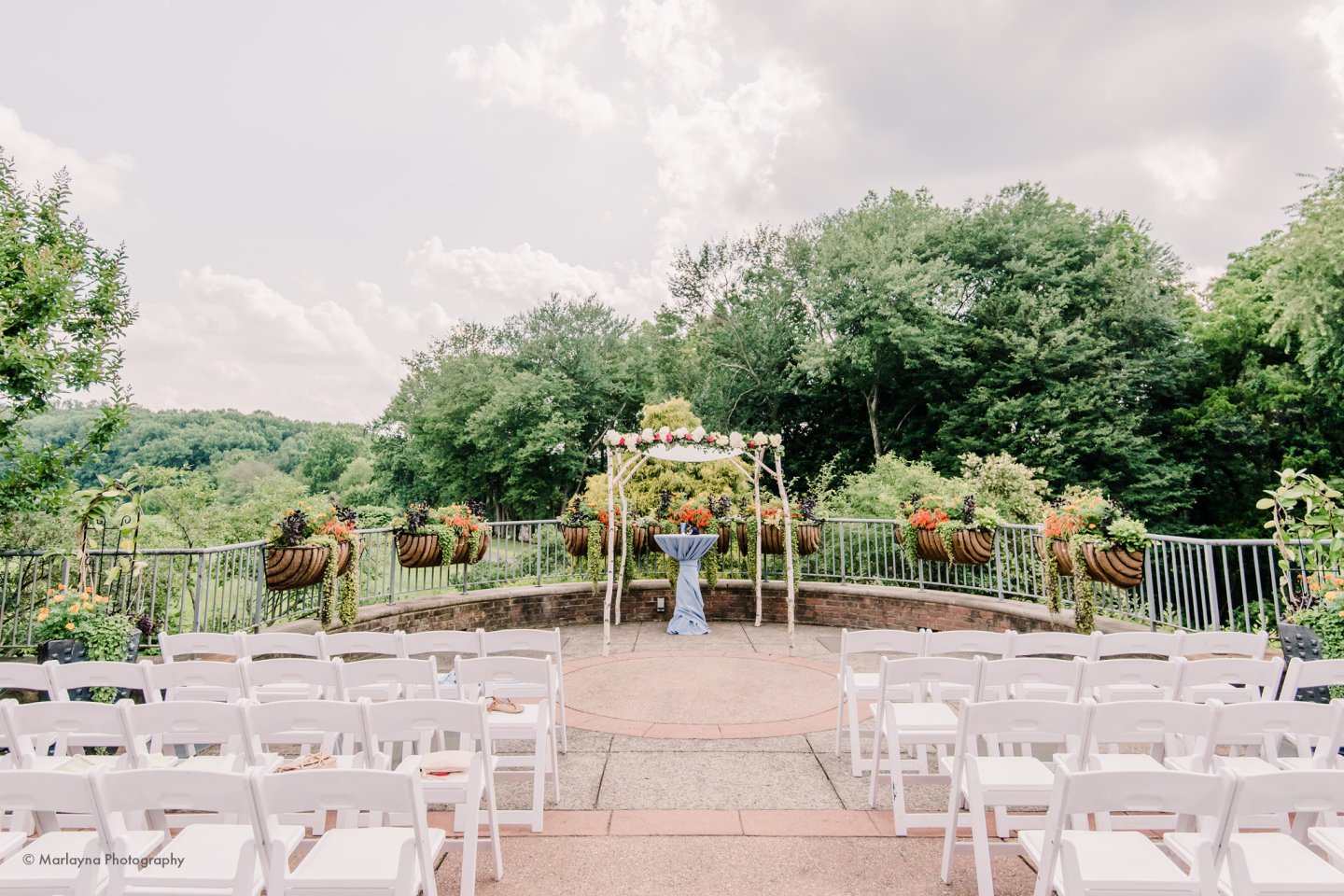 Outdoor wedding setup with white chairs and a floral altar under a cloudy sky.