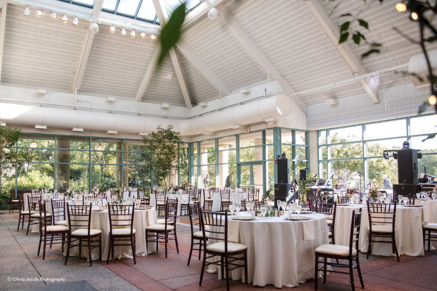Elegant wedding venue with round tables and white chairs in a bright conservatory setting.