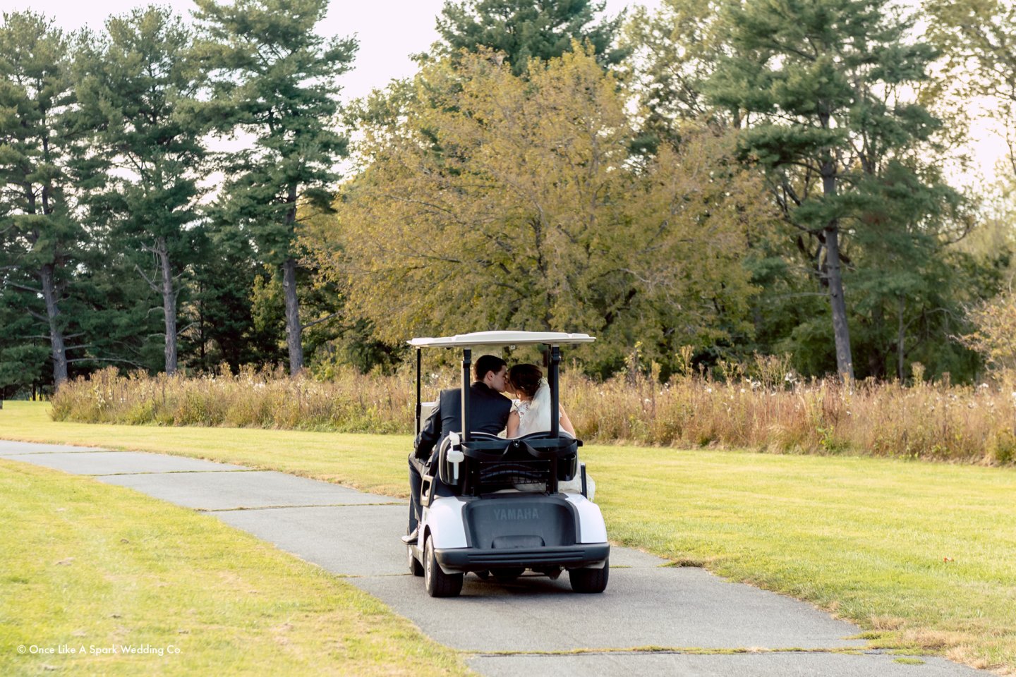 Couple in a golf cart on a scenic path, surrounded by trees.