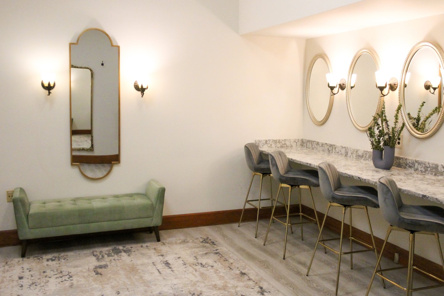 Elegant seating area with mirrors, light fixtures, bar stools, and a green bench.