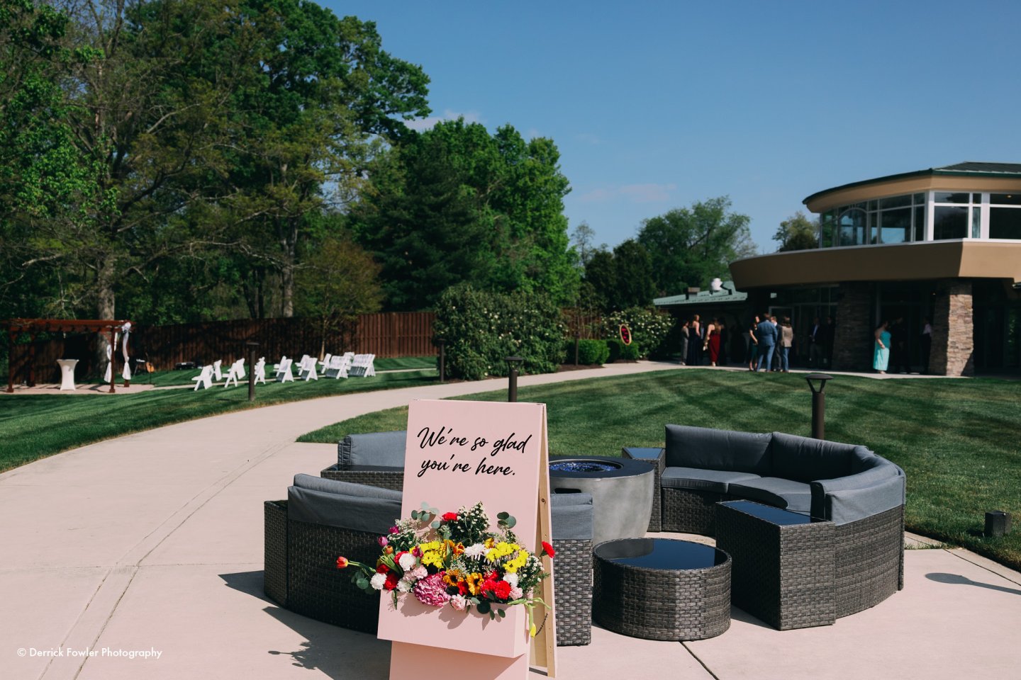 Outdoor wedding setup with patio seating, sign, and guests.