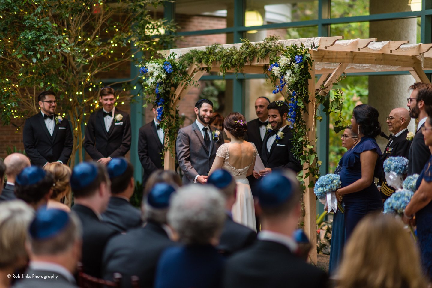 Wedding ceremony under floral arch with guests seated.