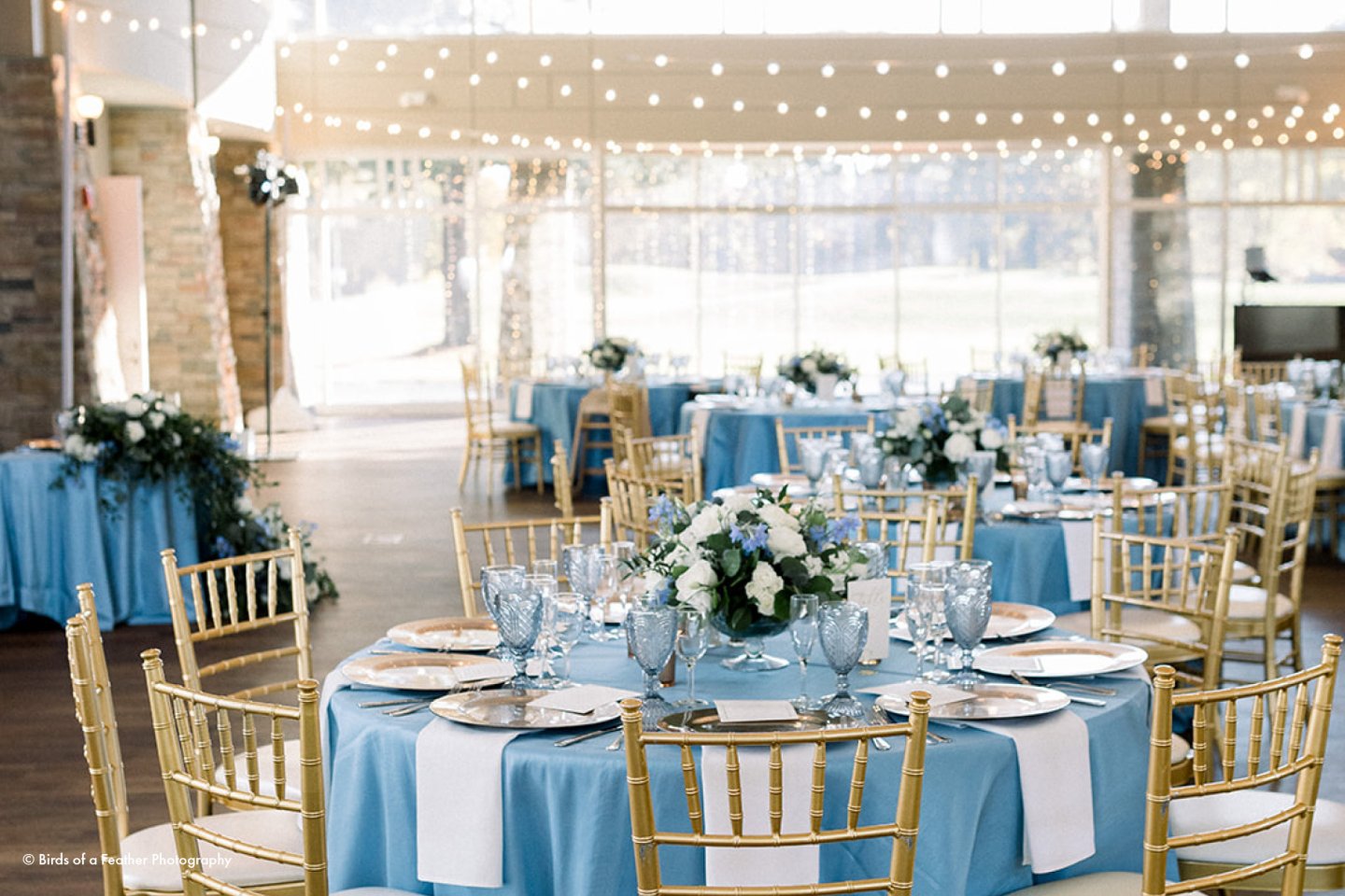 Elegant wedding reception with tables set with blue cloths and golden chairs.