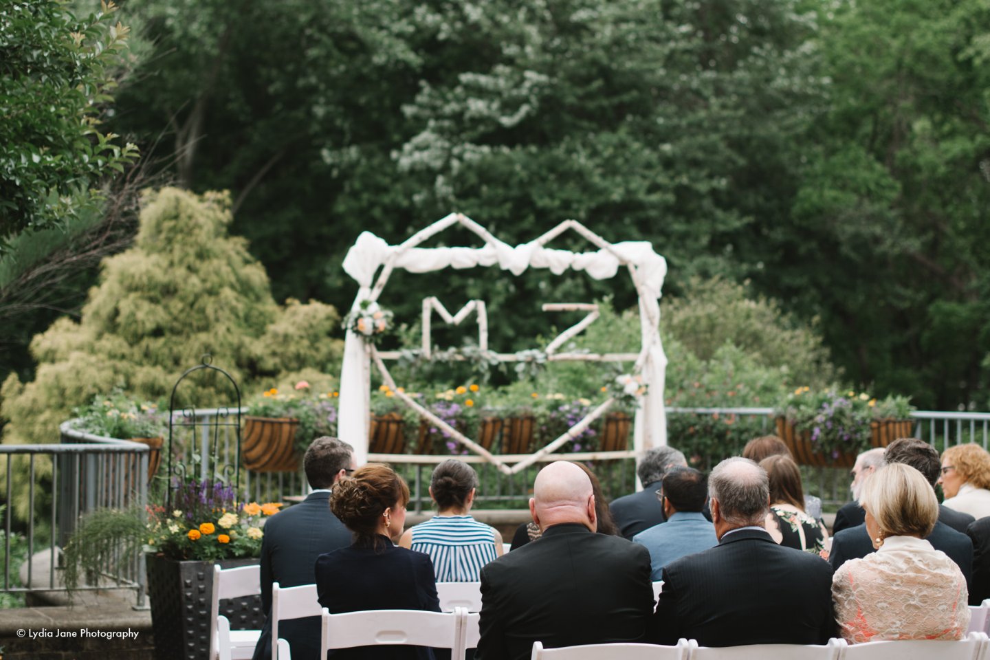 Wedding ceremony with white chairs and floral arch in a garden setting.