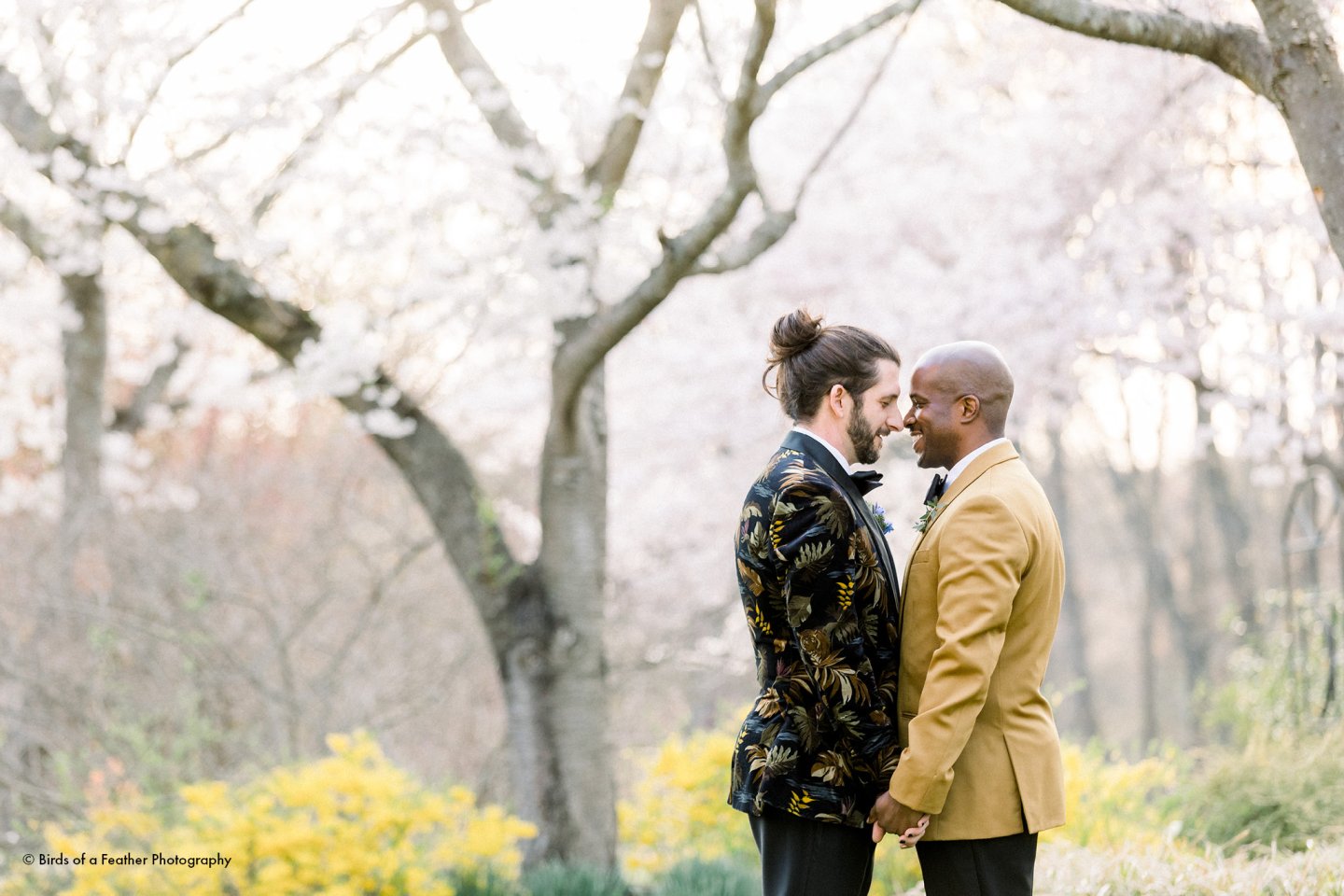 Two men in elegant suits embracing in a blossoming park.
