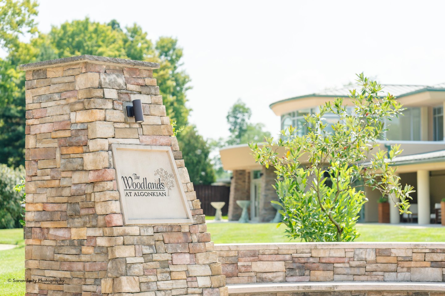 Stone sign, green lawn, and modern building in the background.