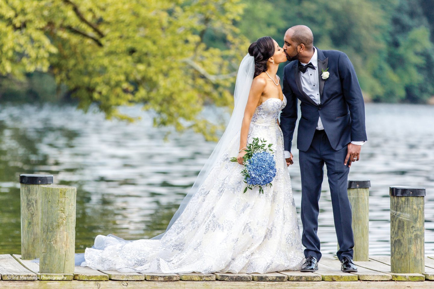 Bride and groom kissing on a lakeside dock, she holds blue flowers.