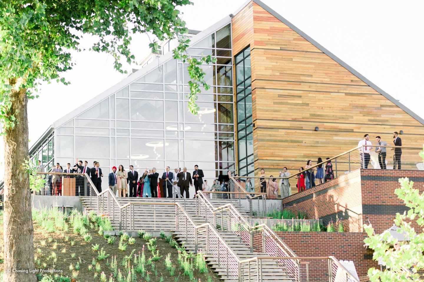 People gathered on a modern building's terrace, with green trees nearby.