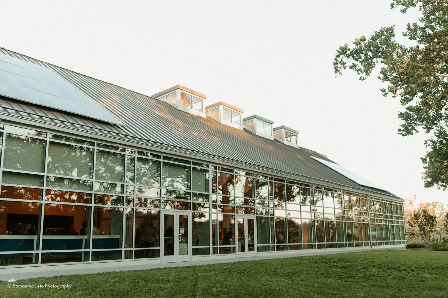 Glass-fronted building with a sloped roof and trees nearby.