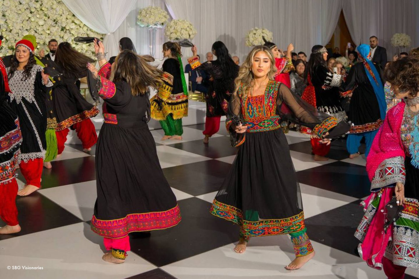 Dancers in colorful traditional attire on a checkered floor.