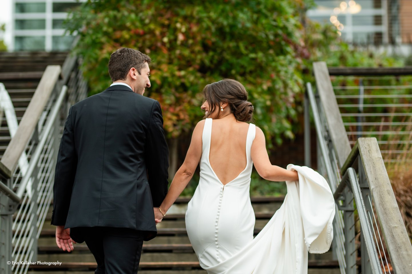 Bride and groom holding hands, walking upstairs, outdoors.