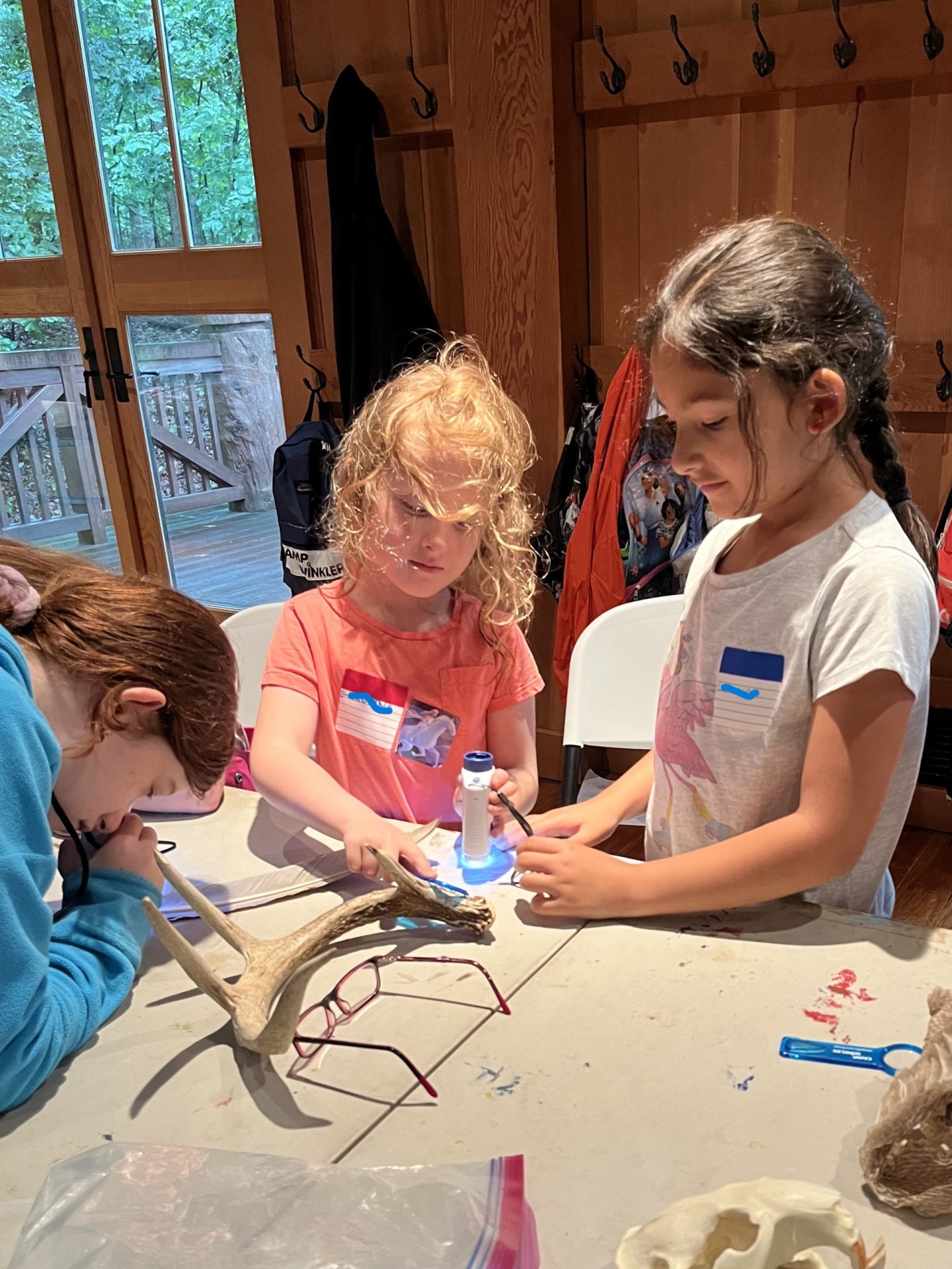 Children crafting at a table indoors, surrounded by art supplies.