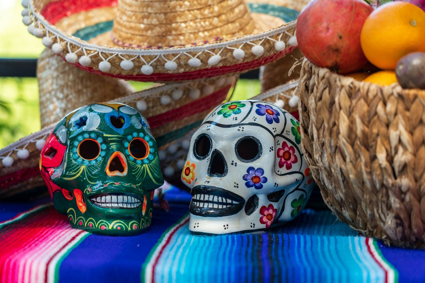 Decorative skulls and fruit basket on colorful textile with sombrero.