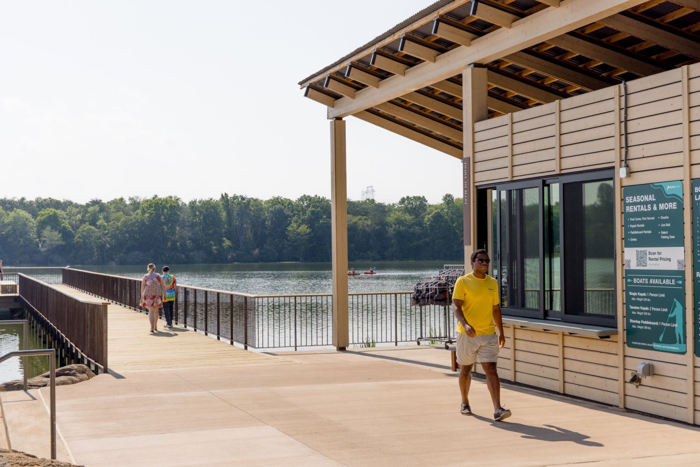 Man in yellow shirt walking by a waterside building on a sunny day.