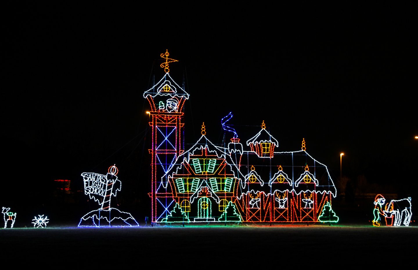 Colorful Christmas light display of a house and tower on a dark background.