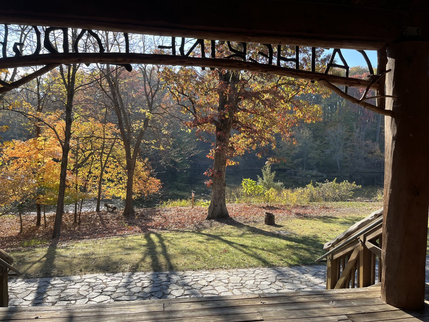 View of autumn trees and path from a shaded porch with wooden railings.