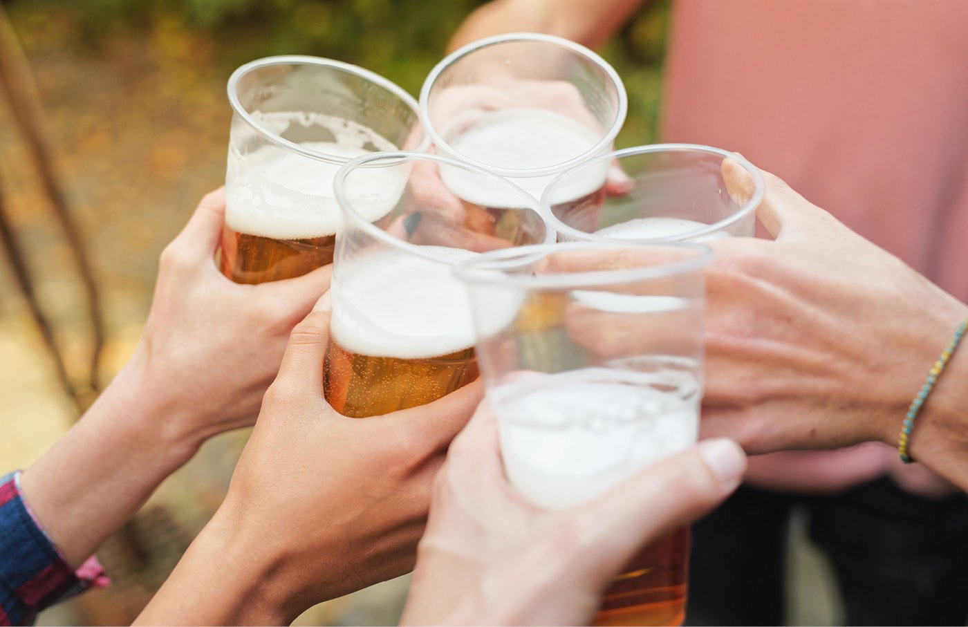 Hands clinking plastic beer cups outdoors.