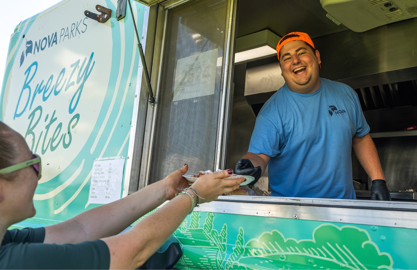 Man handing food from a food truck window, smiling.