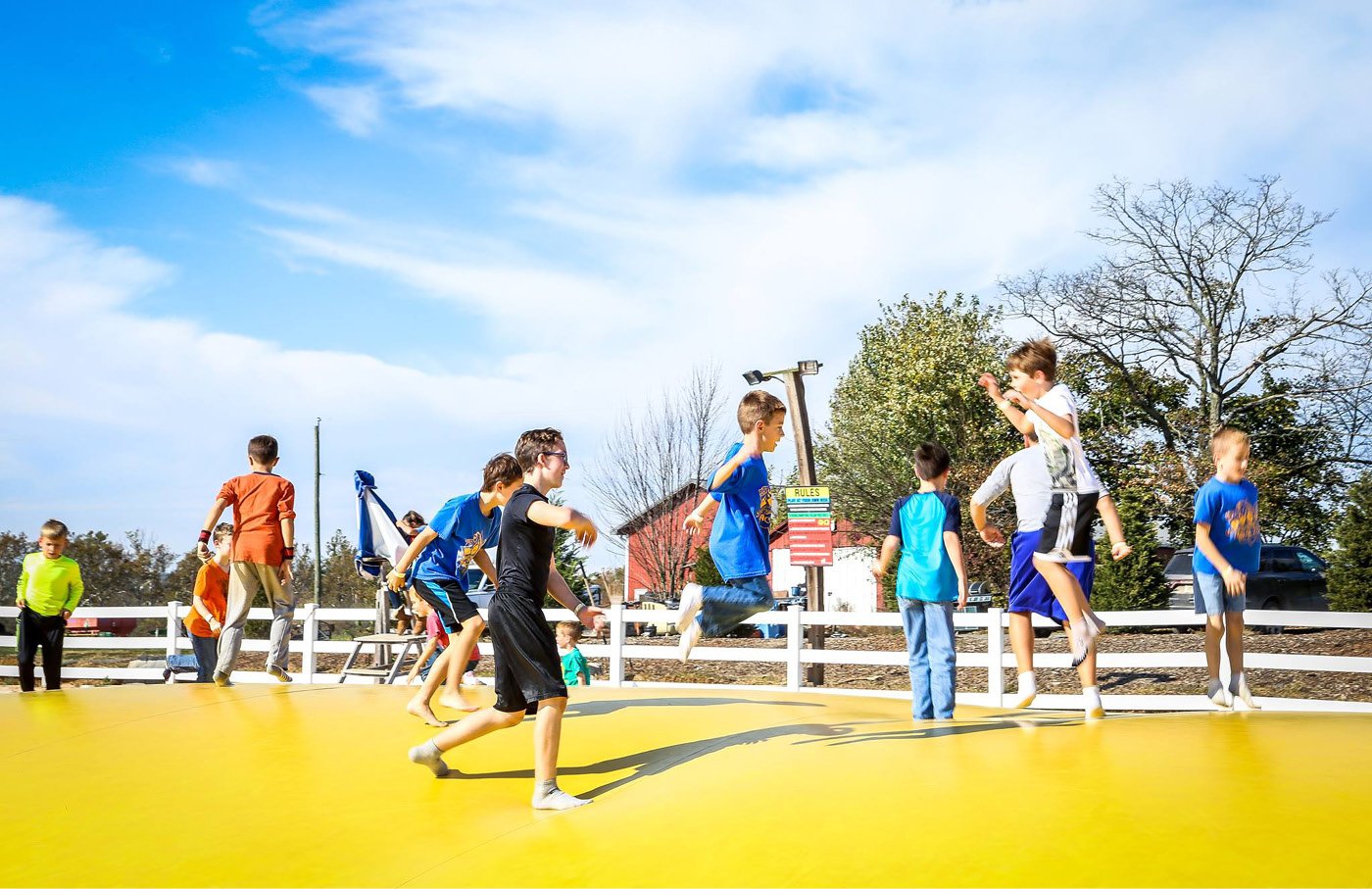 Kids bounce on a large, yellow inflatable platform outdoors under a blue sky.