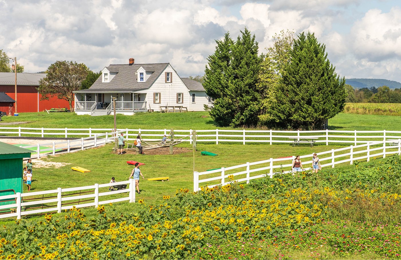 Farmhouse with a white fence, green lawn, and trees under a cloudy sky.