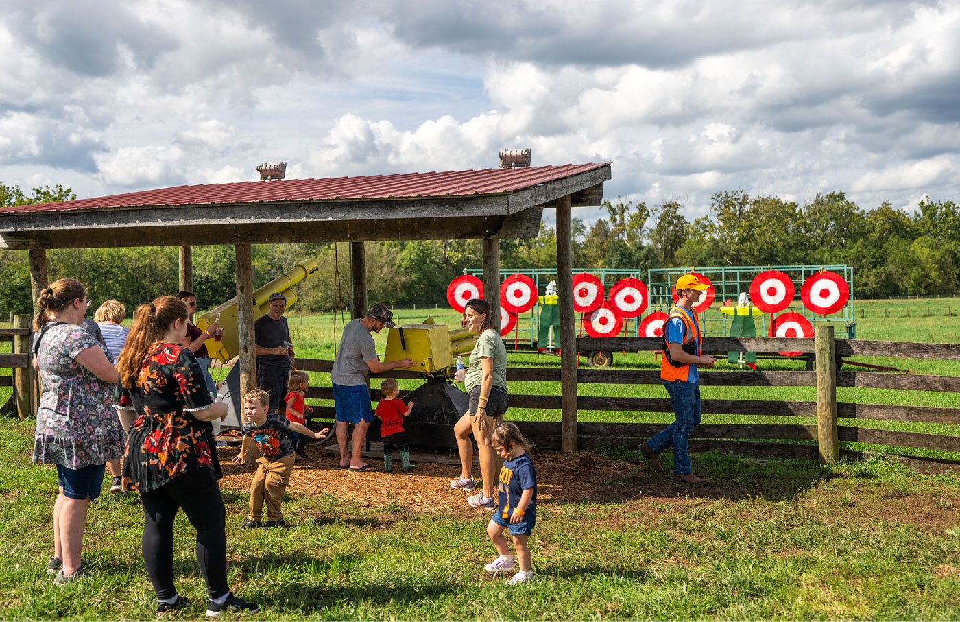 People enjoy an archery range with red target boards under a cloudy sky.