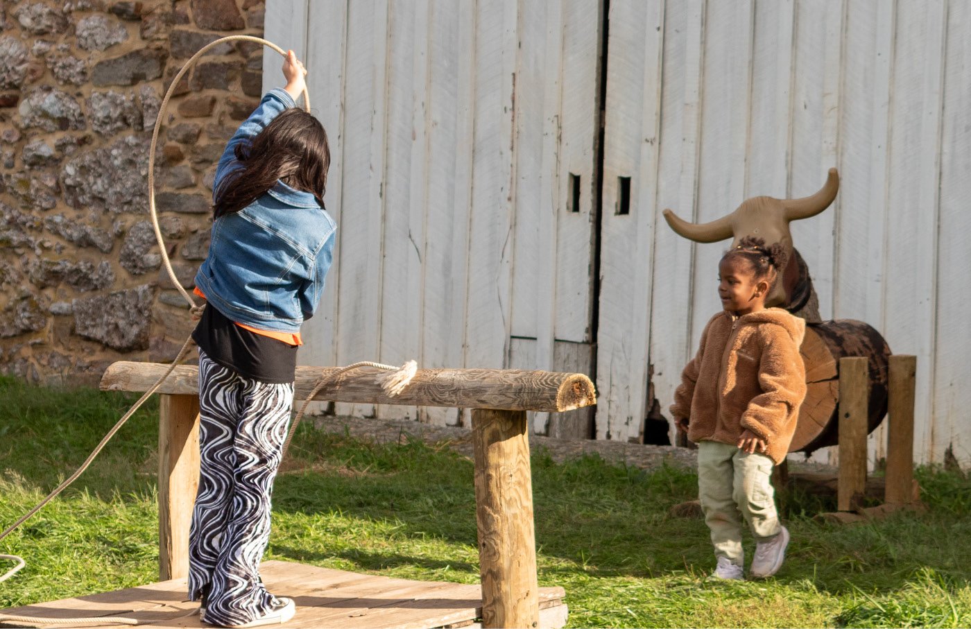 Two children playing with a rope outdoors near a wooden structure.