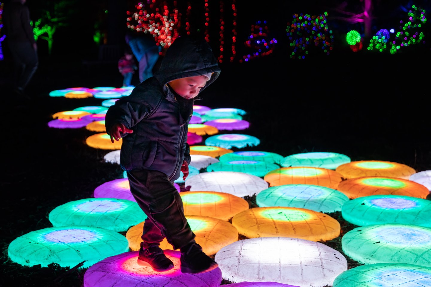 Child walking on colorful illuminated stepping stones at night.