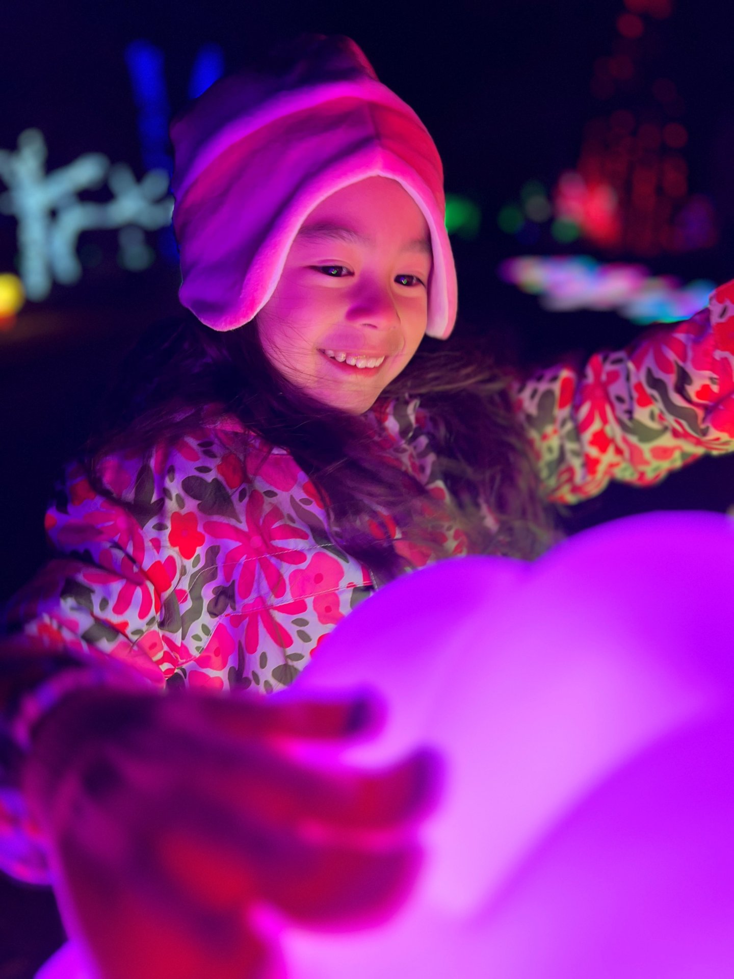 Child in colorful winter clothes and hat, smiling, holding a glowing orb at night.
