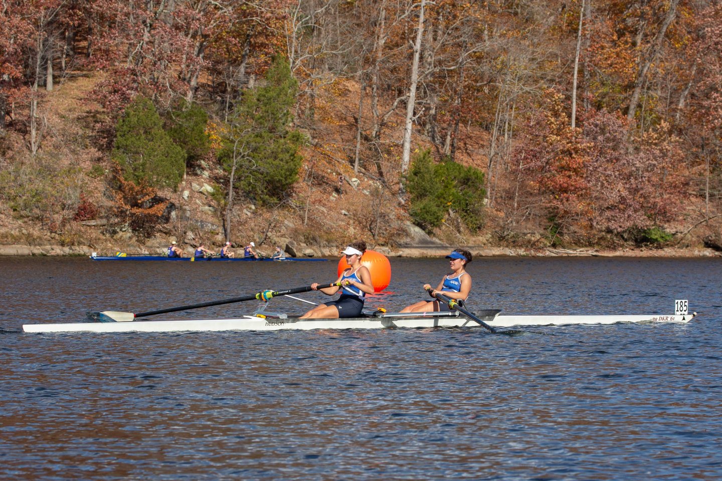 Two people rowing on a lake, surrounded by autumn trees.