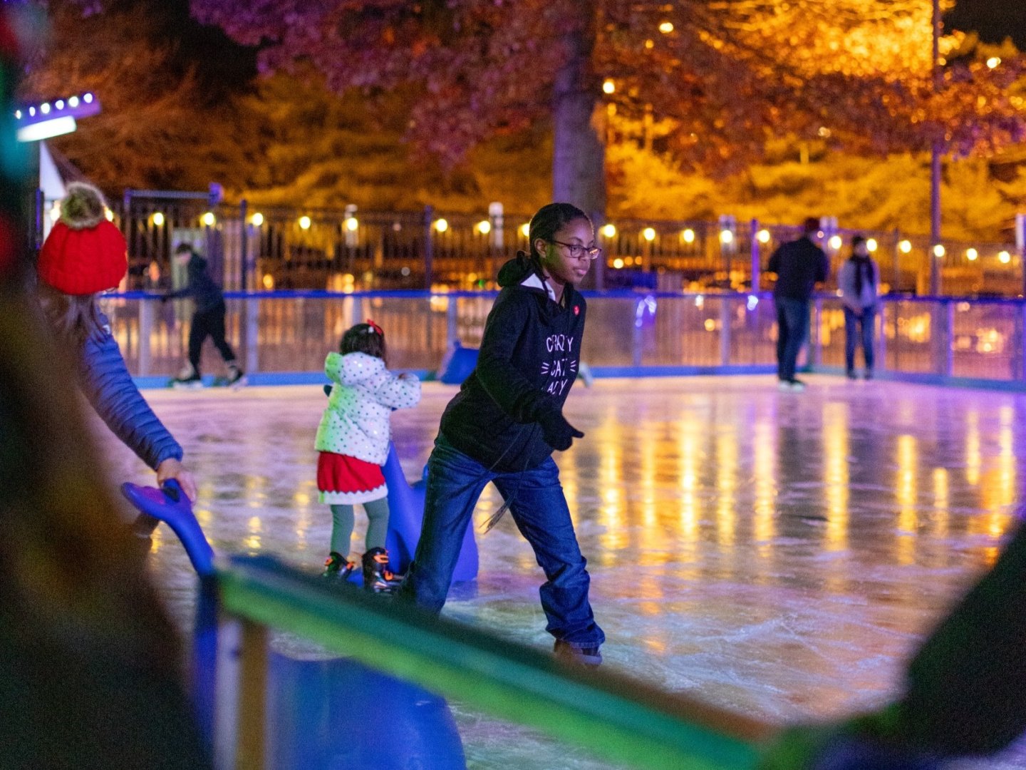 Ice rink with people skating under colorful lights.