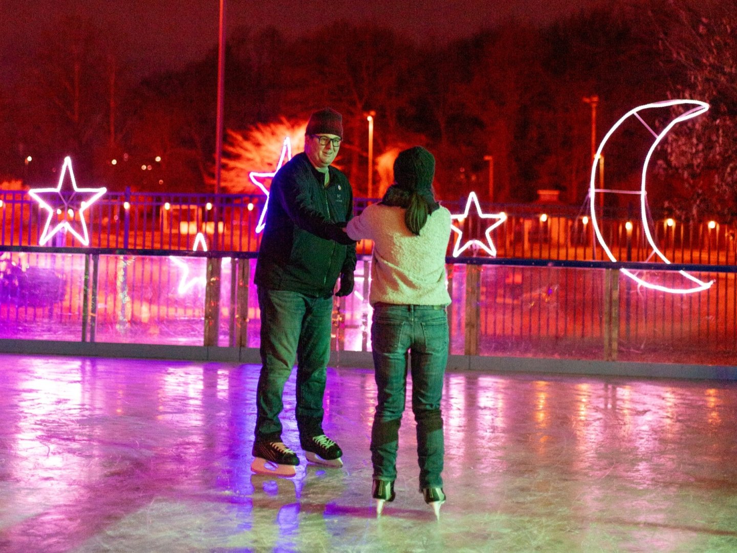 Two people ice skating under colorful neon lights of stars and a crescent moon.