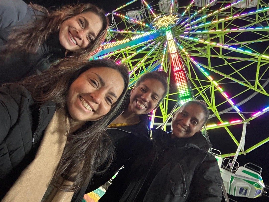 Four people smiling in front of a brightly lit Ferris wheel at night.