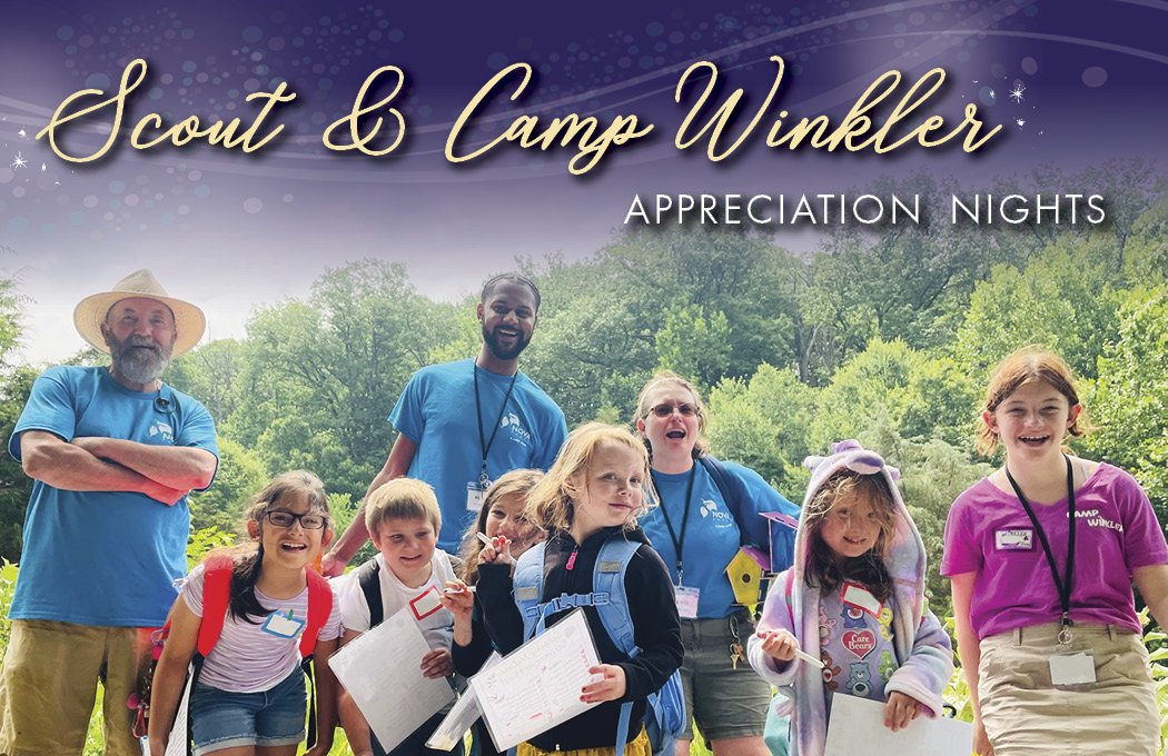 Group of children and adults smiling outdoors, holding papers, against a lush green backdrop.