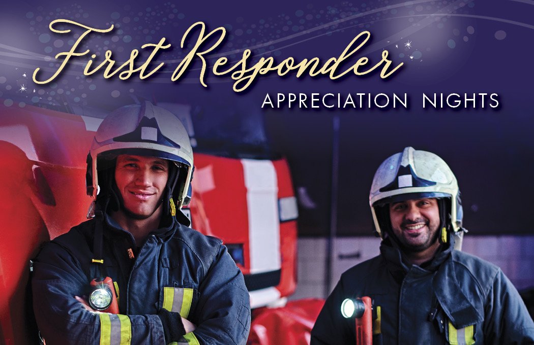 Firefighters smiling in uniform with helmets, red truck in background.