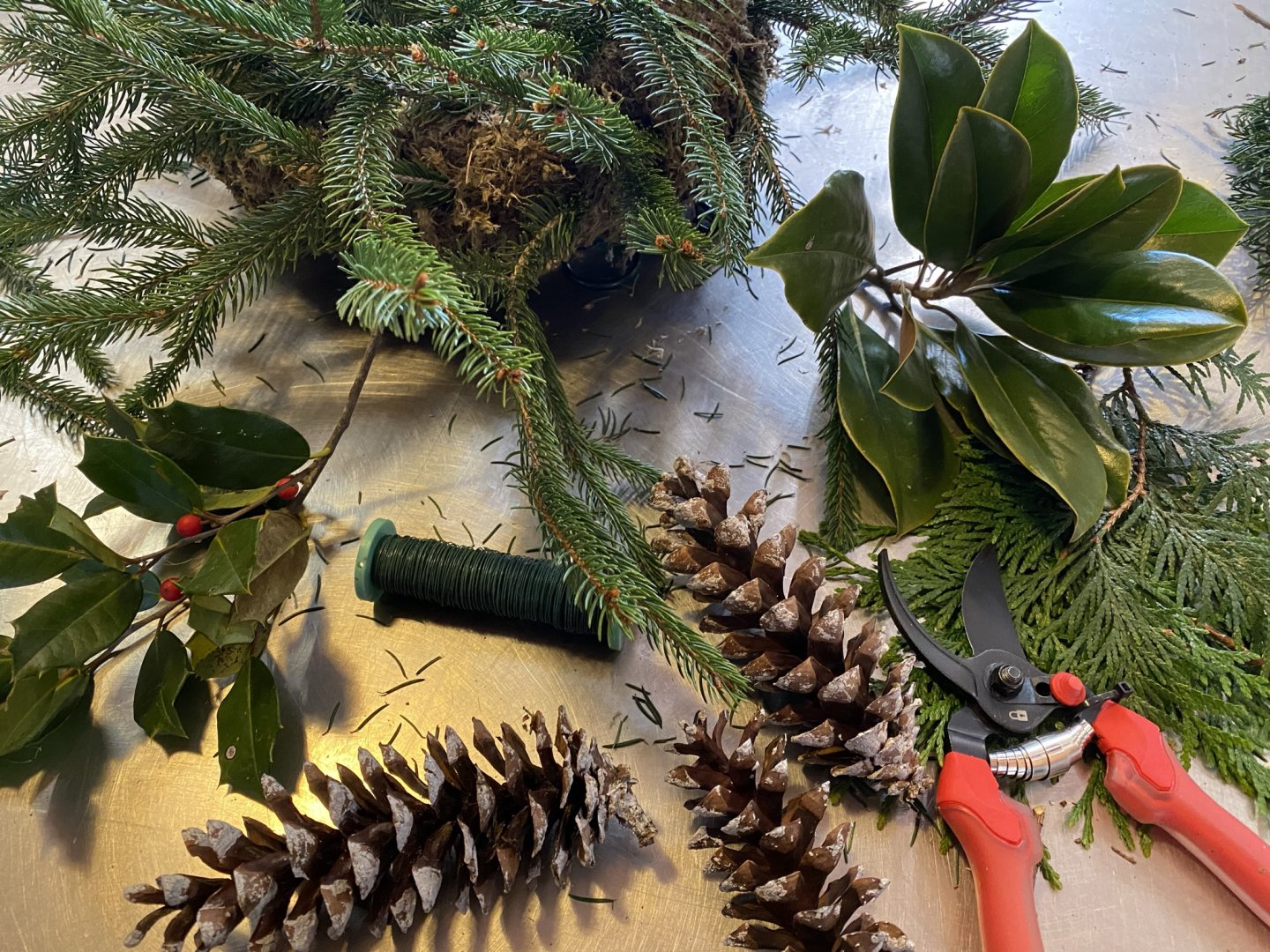 Pinecones, evergreen branches, and pruning shears on a metal surface.