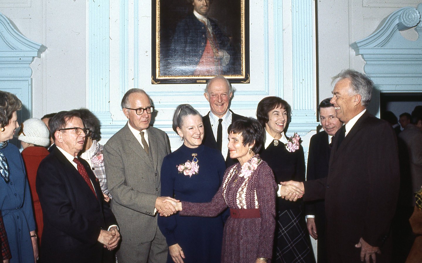 A group of people smiling and shaking hands in a formal room.