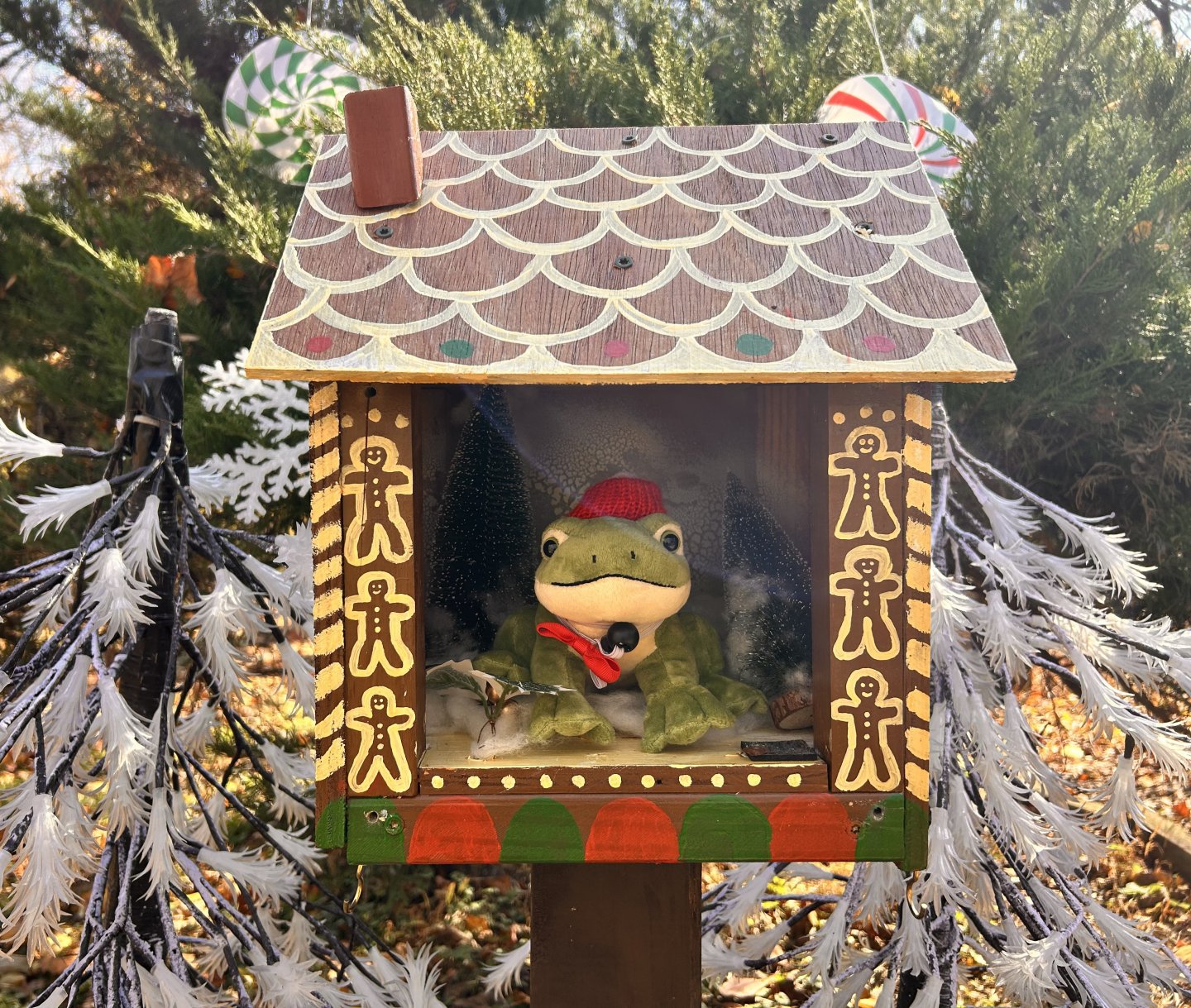 Frog toy in festive birdhouse decorated with gingerbread men.