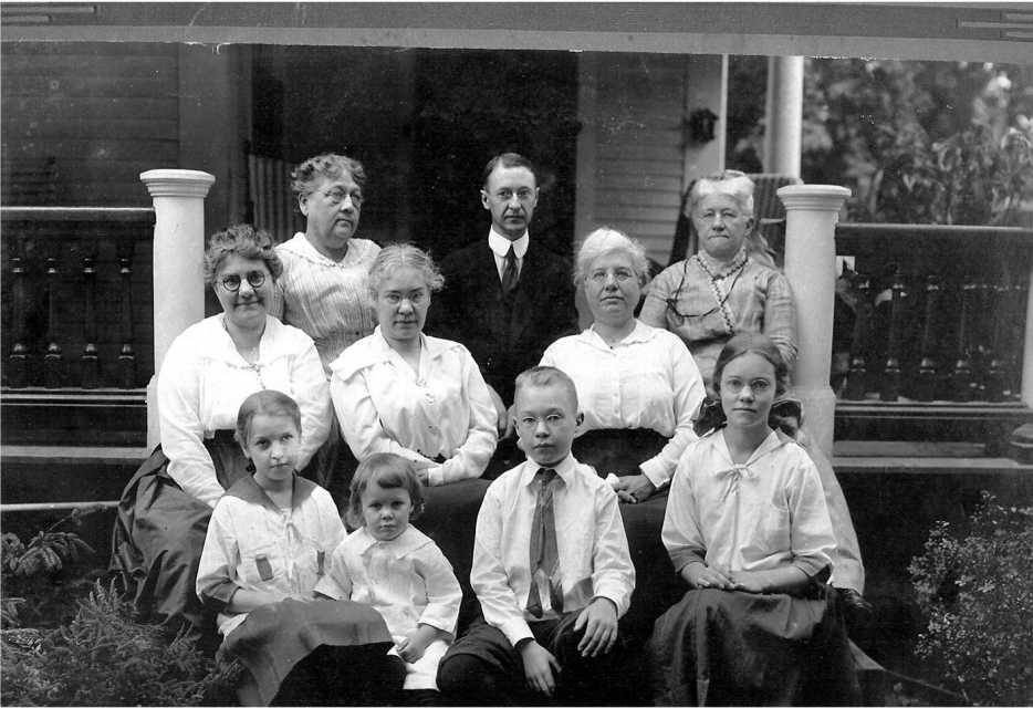 Family group portrait on a porch, vintage clothing, sepia tone.