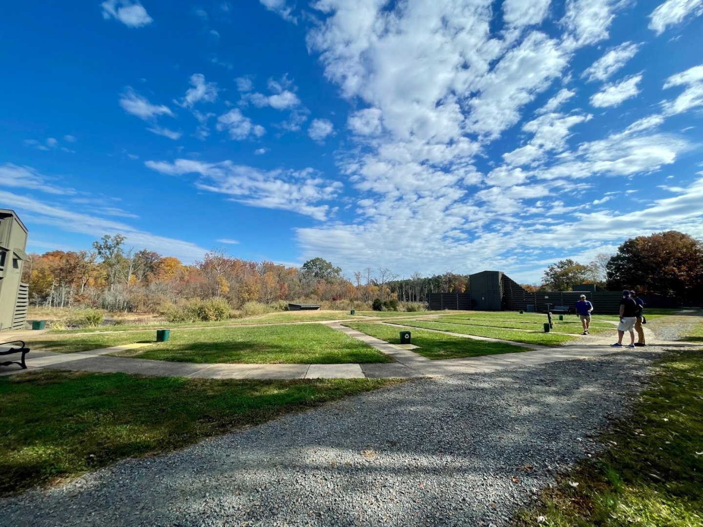 Sunny with trees, blue sky, white clouds; people walking on a path.