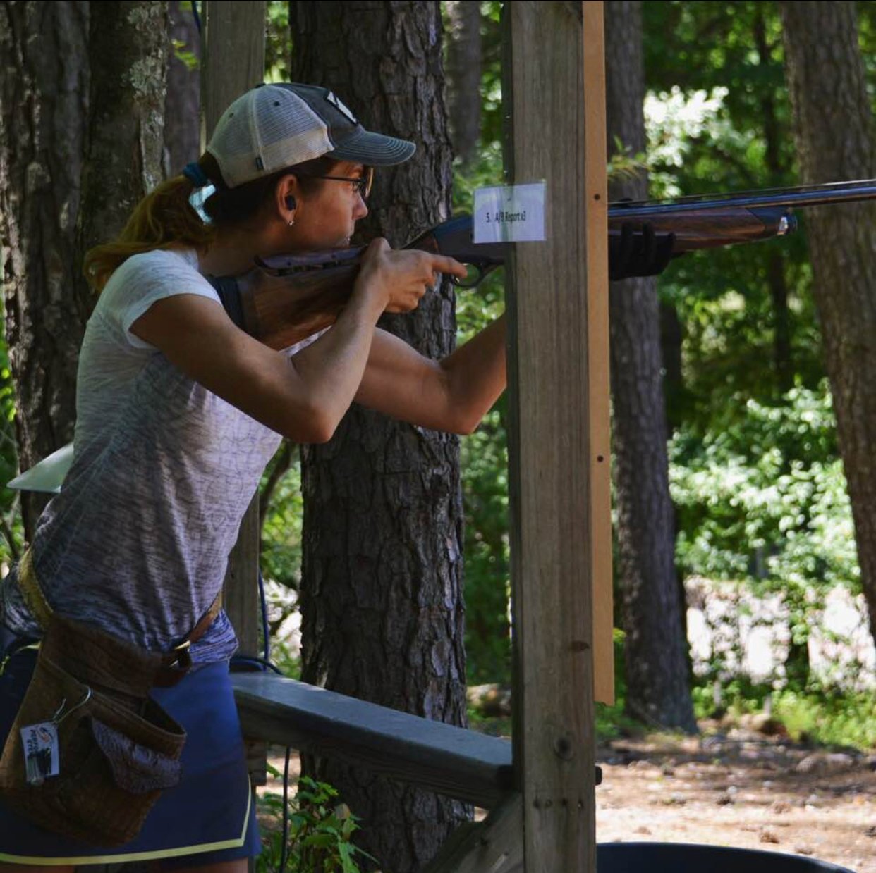Woman aiming a shotgun in a forest setting.