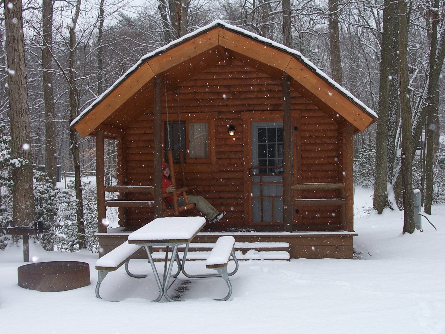 Snow-covered cabin with picnic table in a snowy forest.