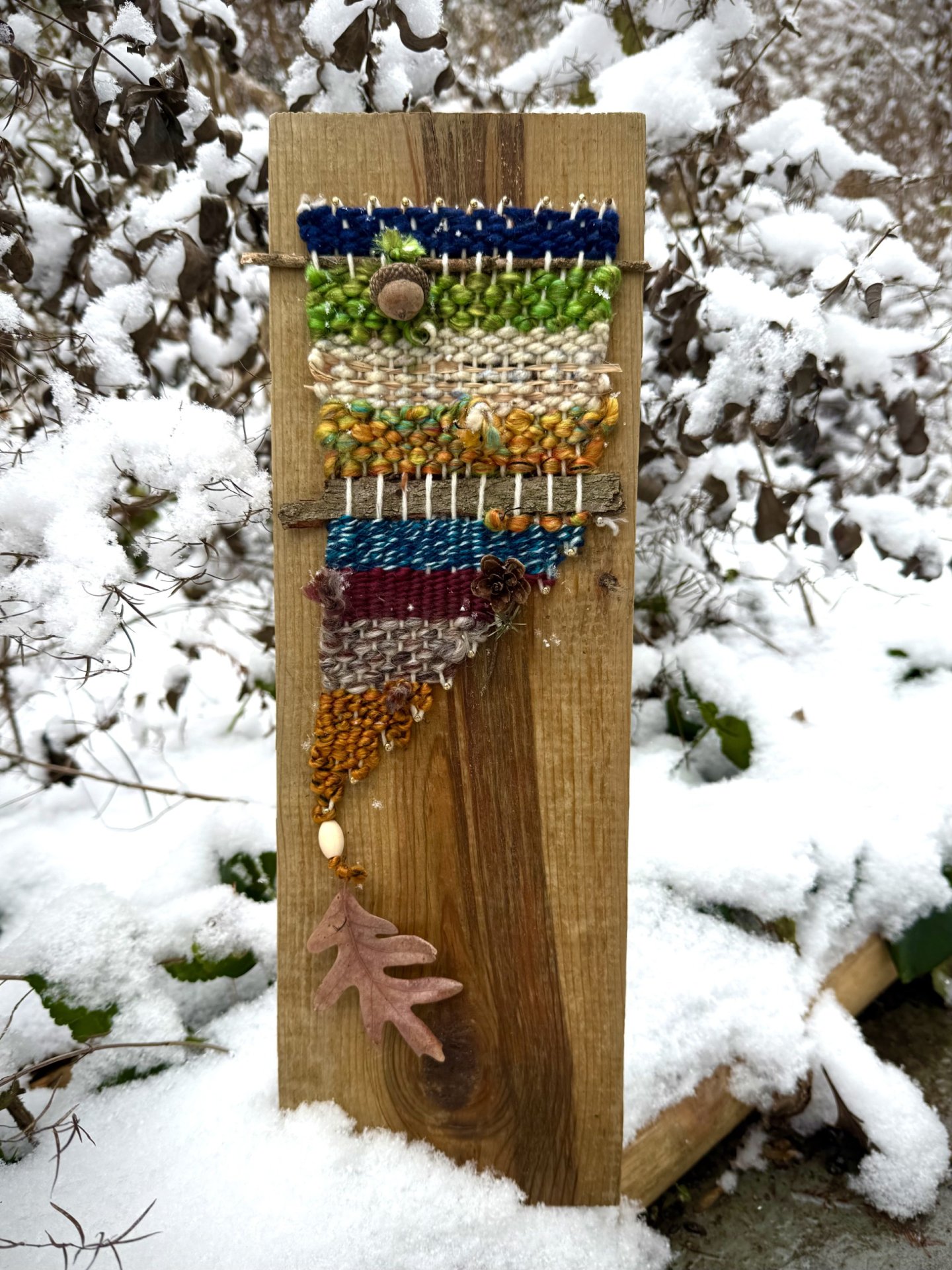 Wooden board with colorful beads and a leaf charm in snowy garden.