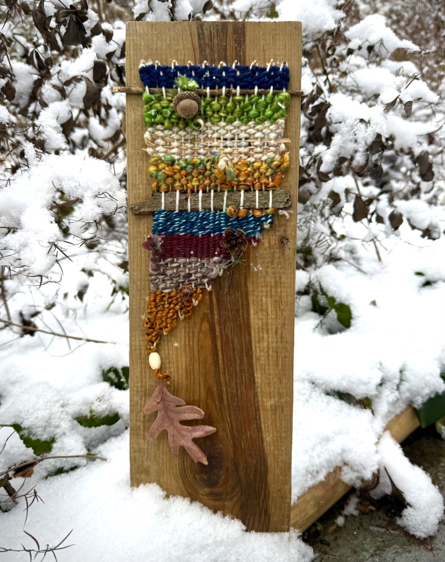 Wood plank with colorful beadwork in snowy garden.
