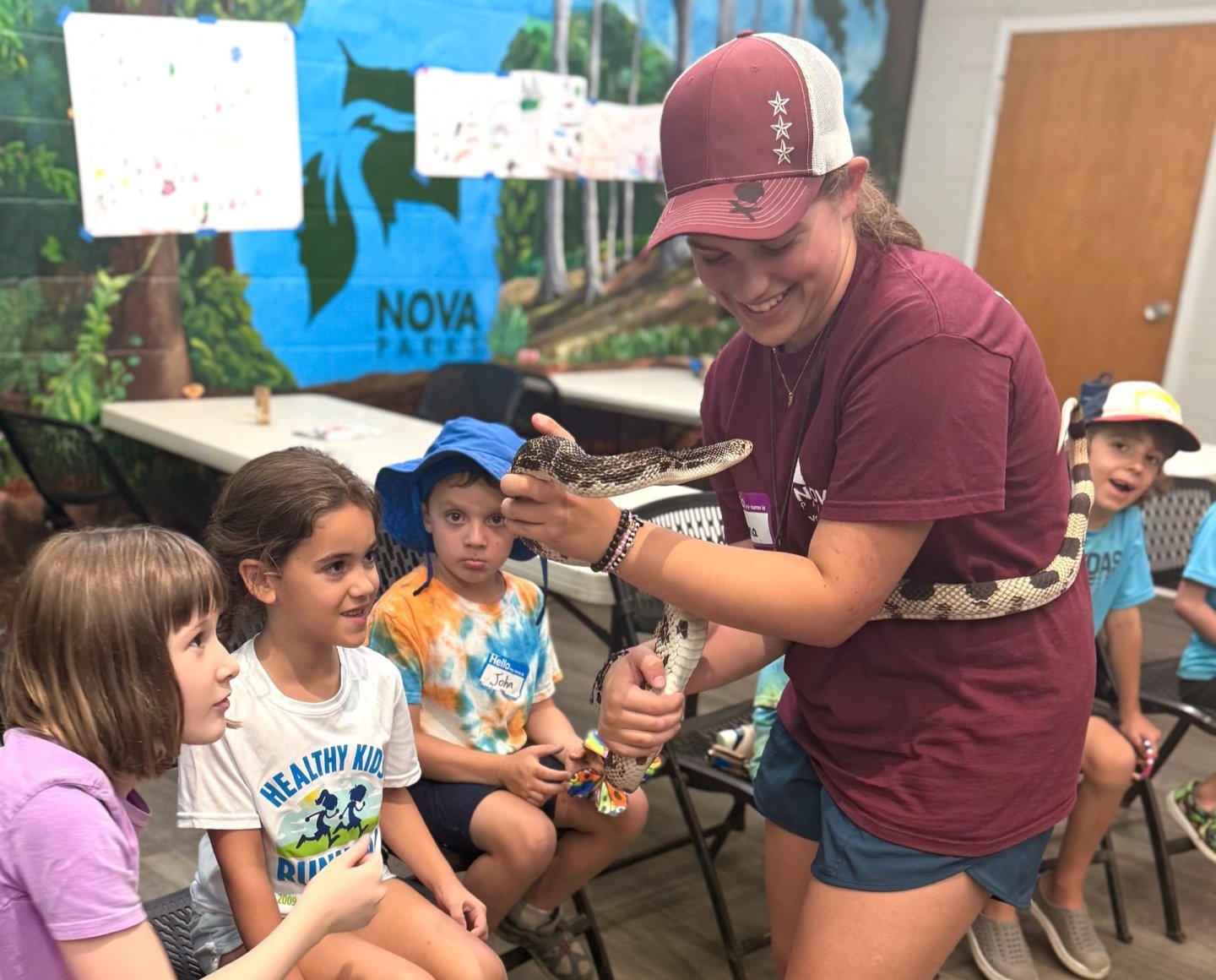 Instructor showing a snake to kids in a classroom with jungle-themed decor.