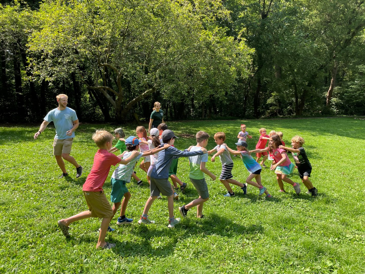 Children playing a game in a sunny park, forming a line holding each other.