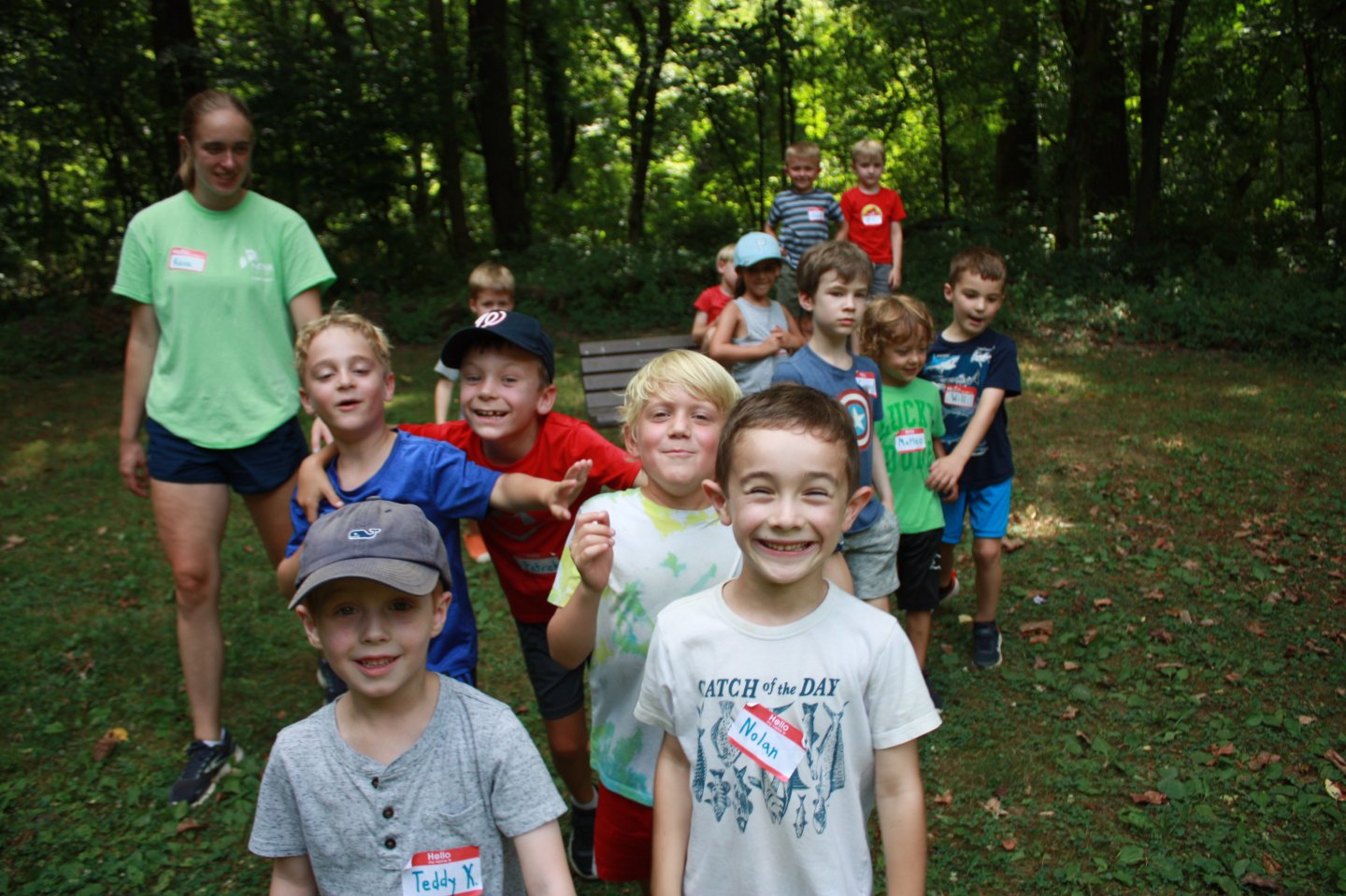 Children lined up outdoors, smiling, with trees in the background.