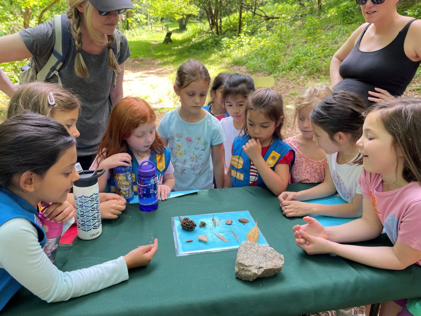 Children gathered around a table examining rocks outdoors.