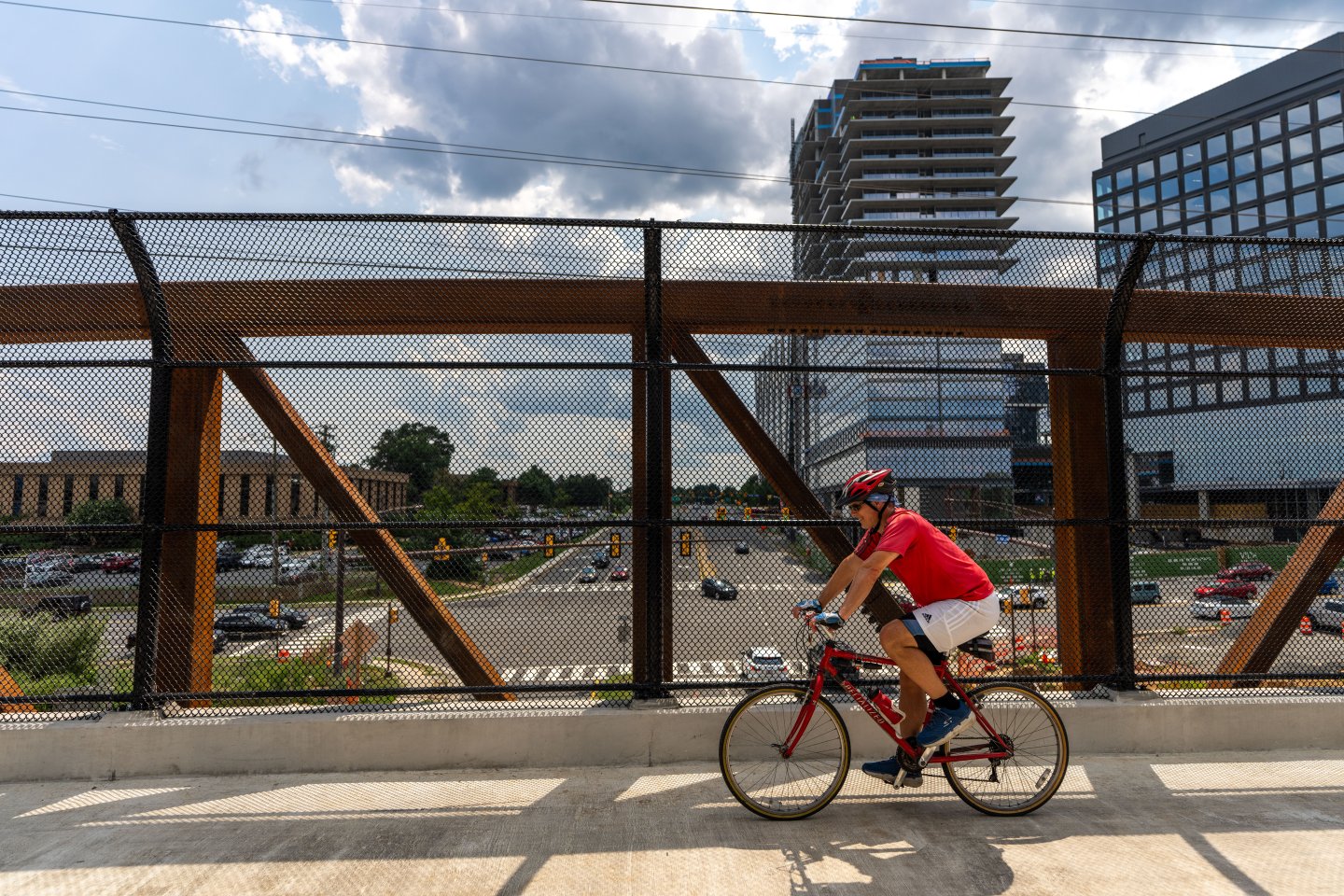 Cyclist on a bridge with city buildings and cloudy sky in the background.